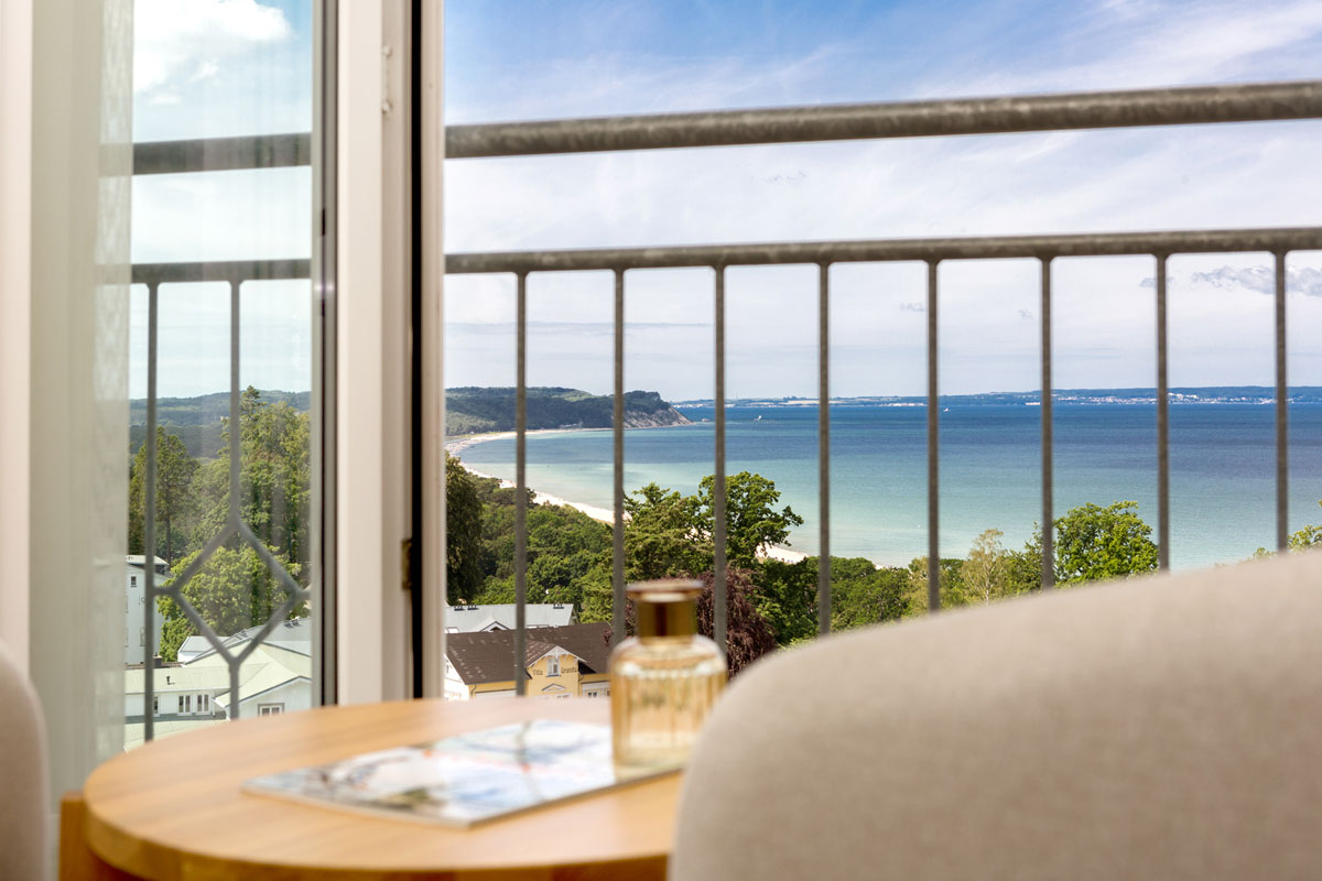 View of the Baltic Sea with sandy beach and green coastal landscape from the hotel room balcony of the Vju Hotel Rügen.