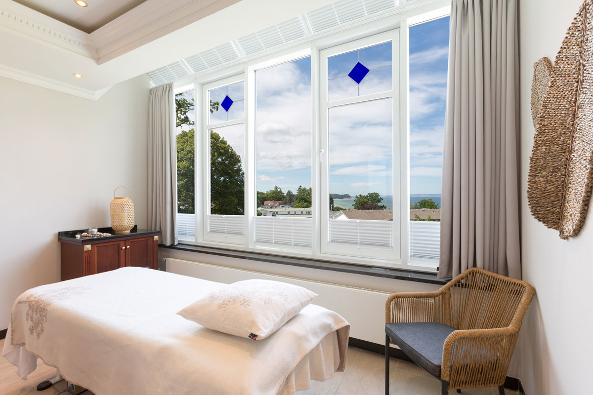 Treatment room with large windows overlooking the sea and the green surroundings of the Vju Hotel Rügen.