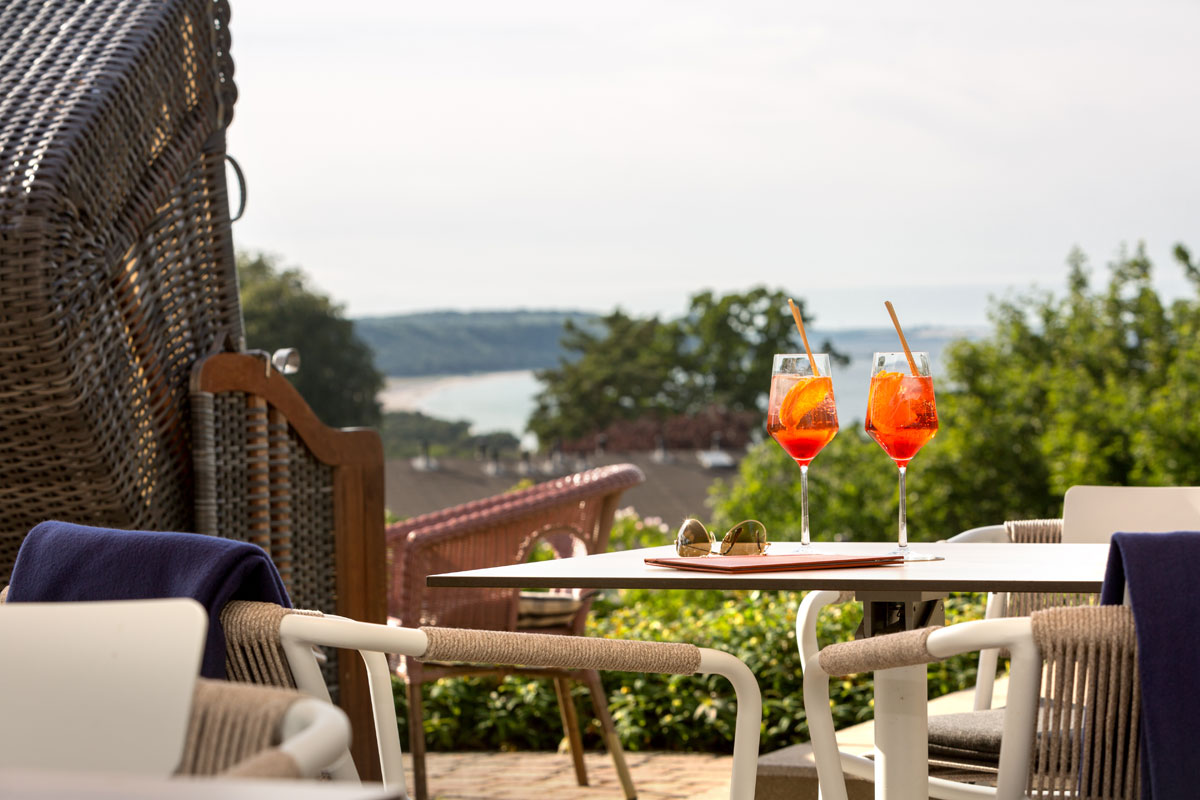 Sonnige Hotelterrasse mit Rattanmöbeln, Aperitif-Gläsern und herrlichem Blick über die Küste im Urlaub im Vju Hotel.