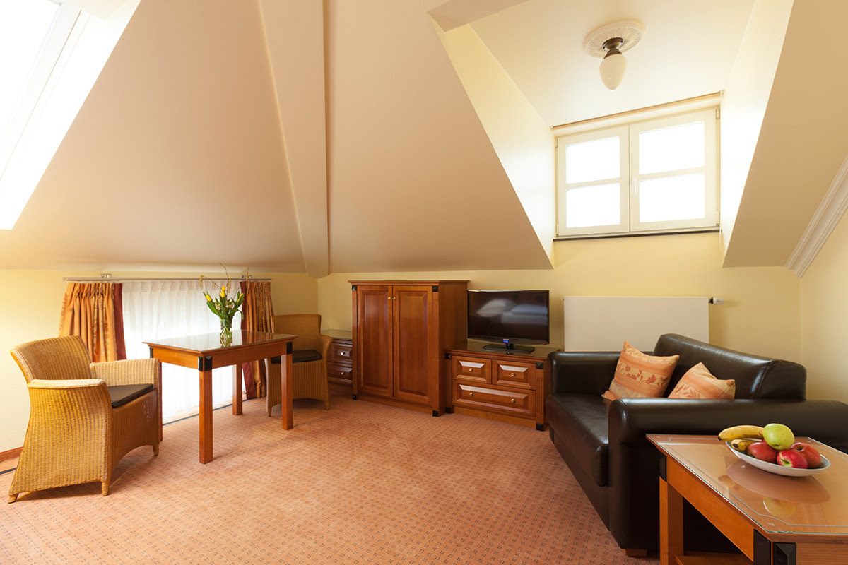 Komfortable Sitzecke mit Ledersofa, Holztisch und Fernseher im 2-Raum-Zimmer in den Dependancen im Vju Hotel auf Rügen.