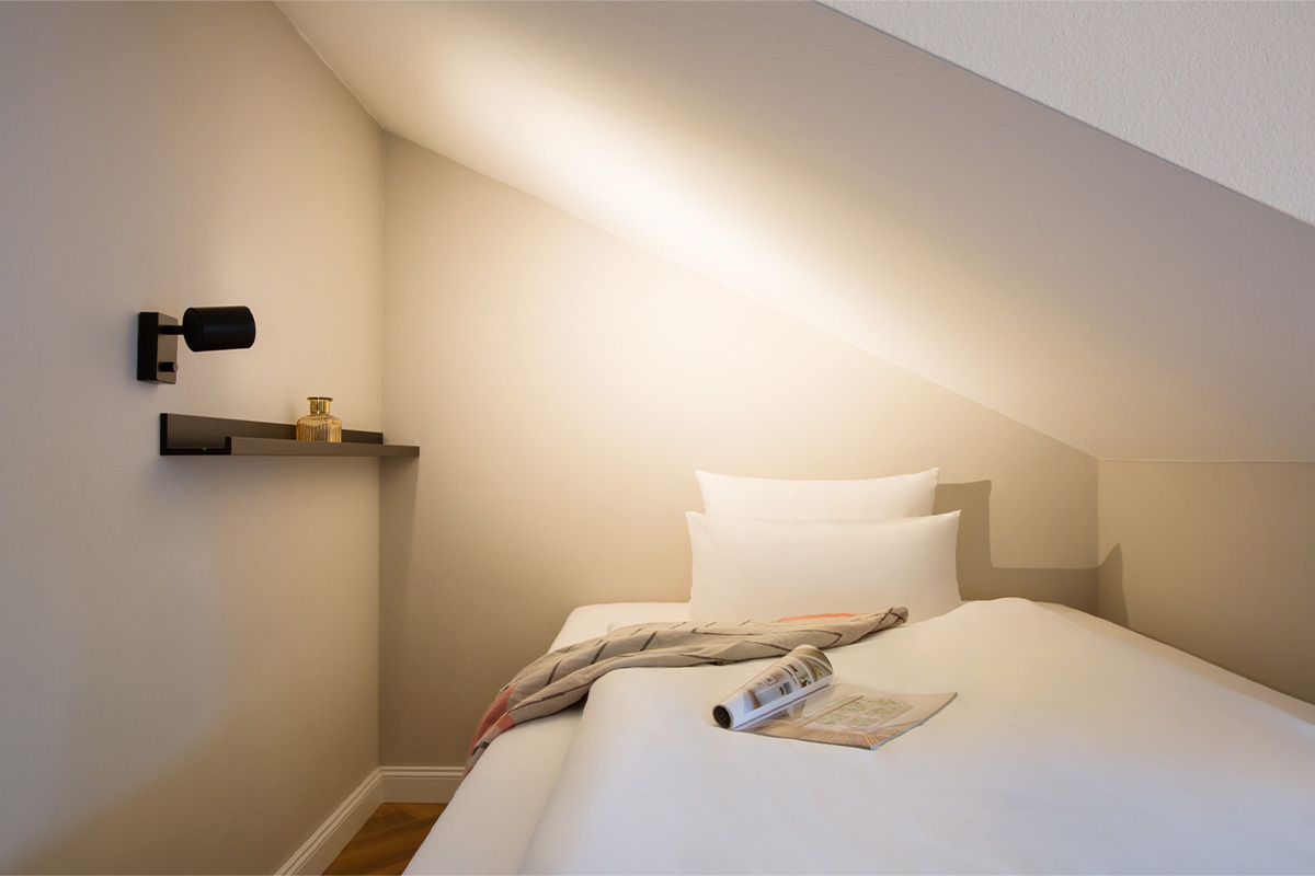 Gemütliches Einzelbett unter einer Dachschräge im Queensize-Einzelzimmer des Vju Hotels.