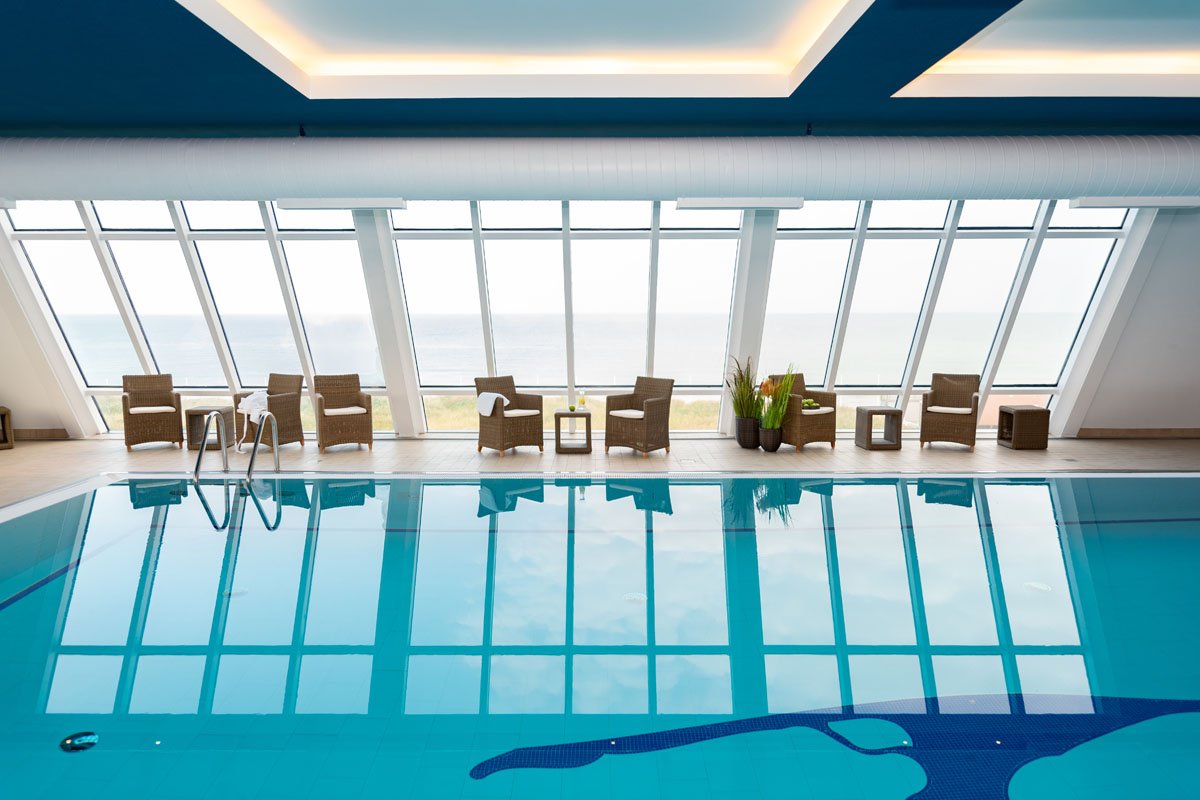 Indoor pool with large glass windows and a view of the North Sea, perfect for vacation packages from the Wyn. Strandhotel on Sylt.