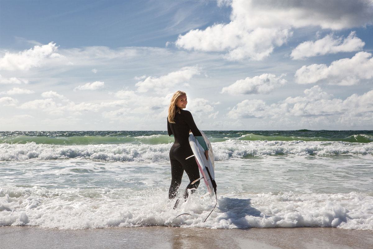 Surfer in wetsuit with surfboard standing in the waves on an active vacation at the Wyn. Strandhotel on Sylt.