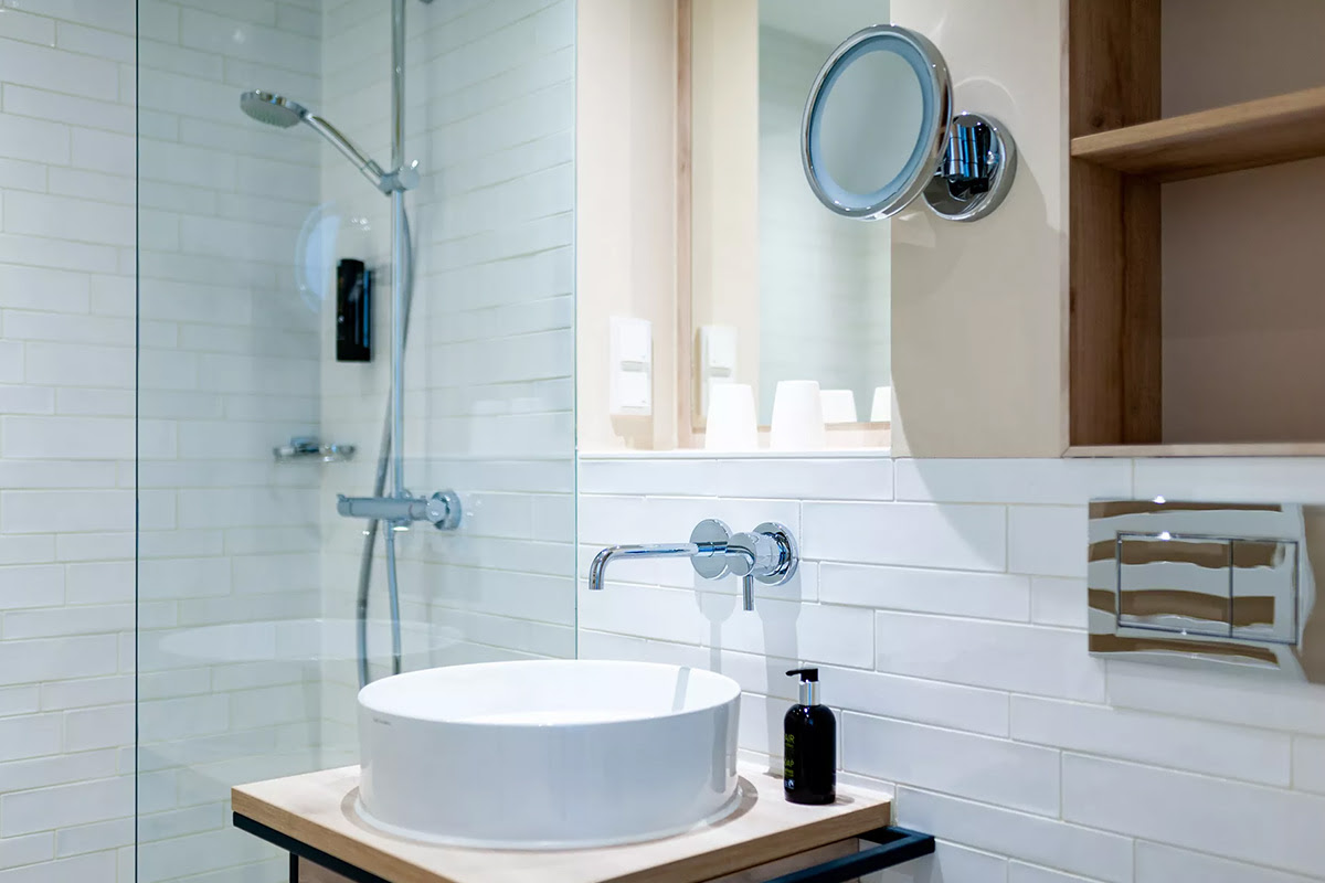 Bright bathroom in the Strandhafer Suite with rain shower, washbasin, mirror and modern accents in the Wyn. Strandhotel.