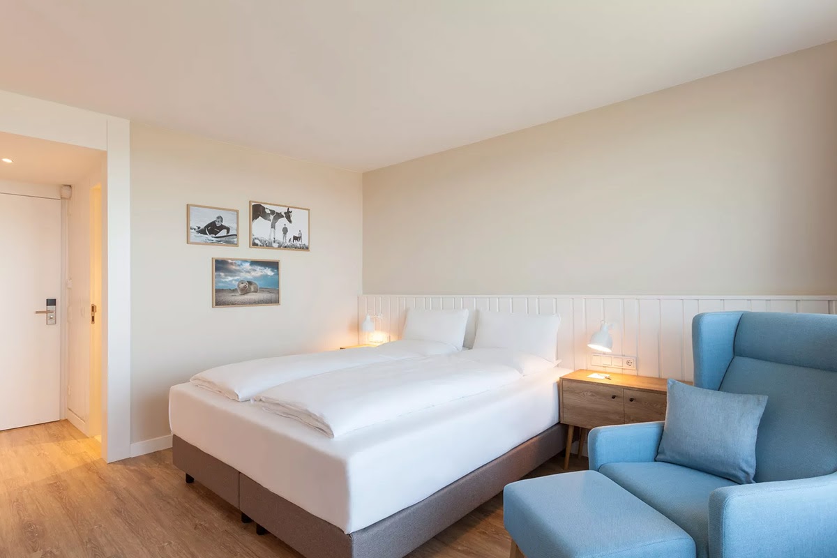 Bright hotel room Buhne in the Wyn. Strandhotel with large double bed, bedside table, reading lamp and comfortable armchair.
