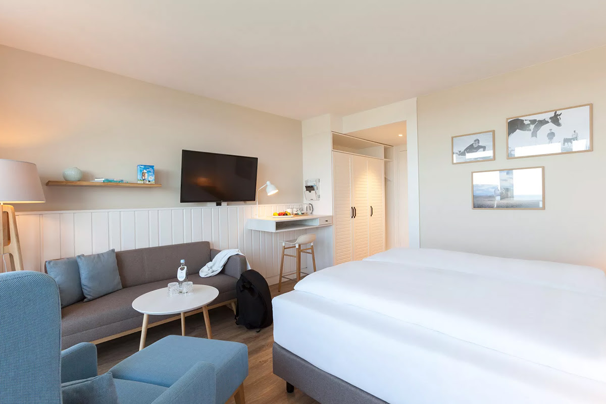 Room Buhne with large bed, cozy sitting area, wall paintings and desk area in the Wyn. Strandhotel on Sylt.