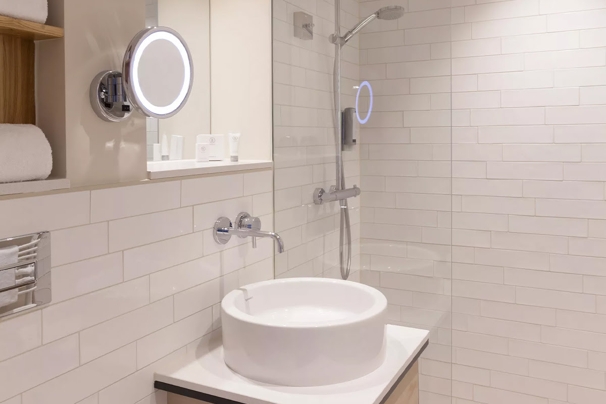 Modern bathroom with round washbasin, glass shower and illuminated vanity mirror in the Buhne room of the Wyn. Strandhotel.
