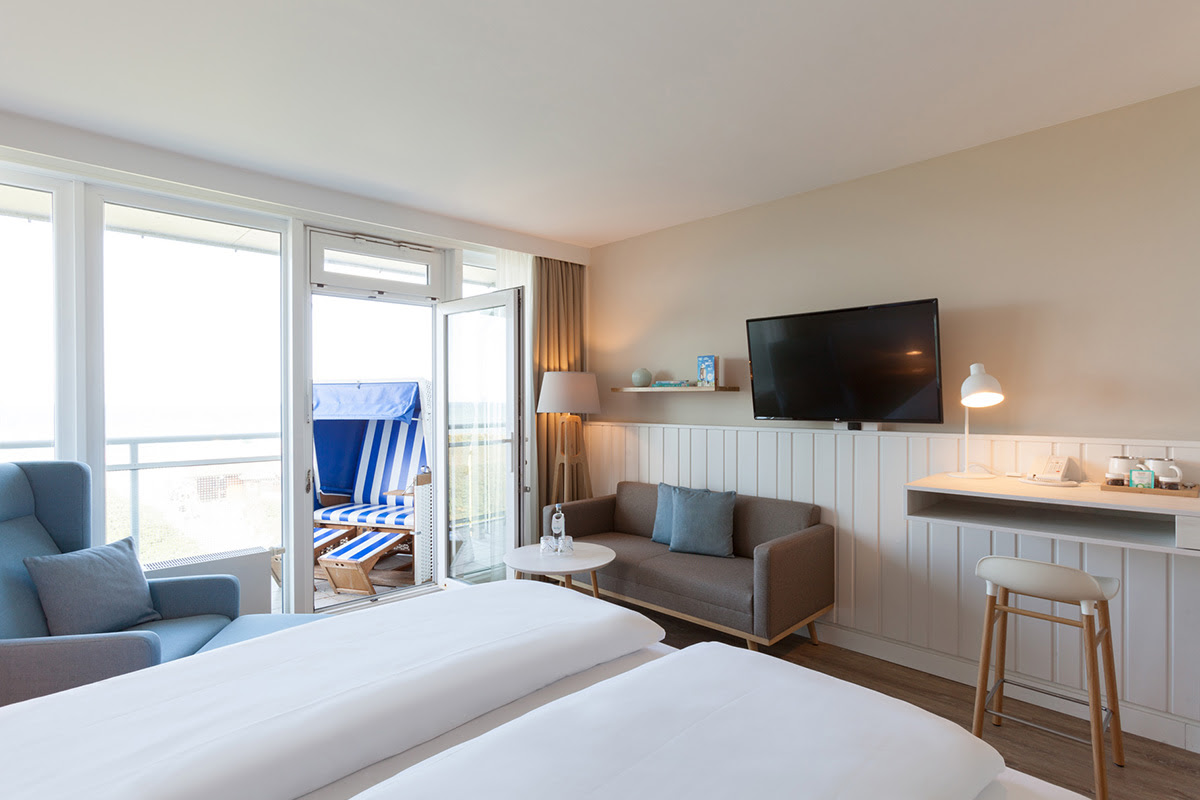 Modern furnished hotel room Buhne with sofa, TV and access to the balcony with beach chair in the Wyn. Strandhotel.