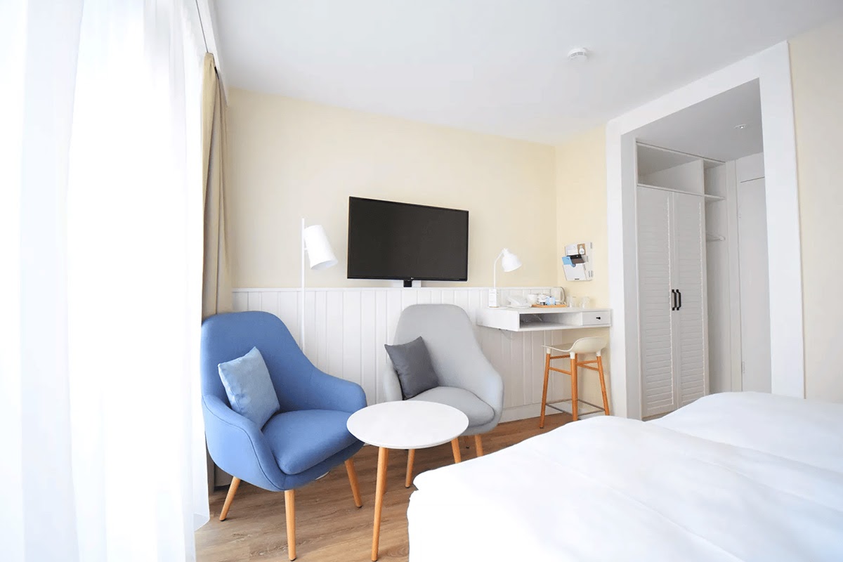 Bright seating area in the “Land in sight” hotel room at the Wyn. Strandhotel with two armchairs, side table and natural light.