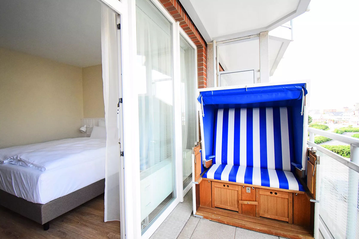Room “Land in Sicht” in the Wyn. Strandhotel with double bed and direct access to the balcony with blue and white beach chair.
