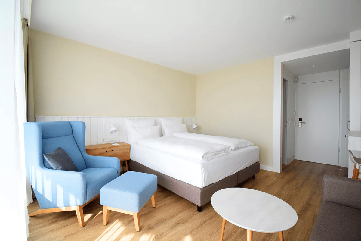 Bright, modernly furnished Muschelsucher room with cozy bed and blue wing chair in the Wyn. Strandhotel.