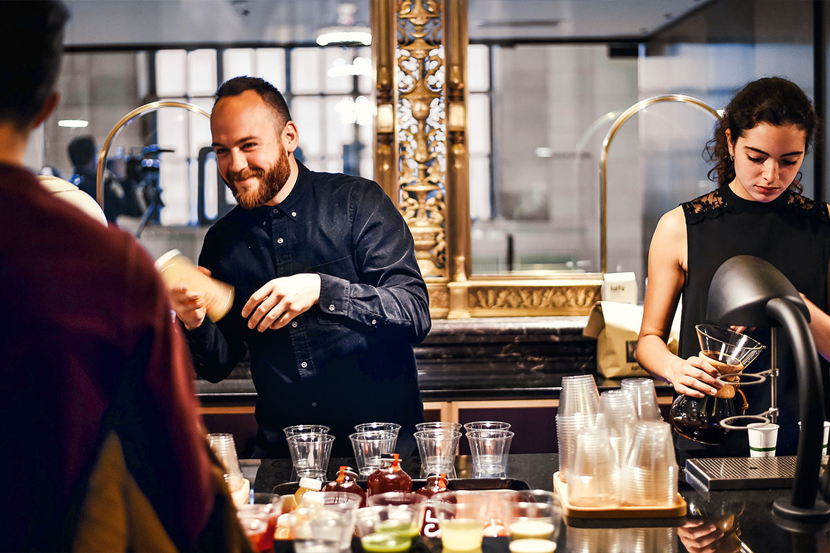 Barista und Mitarbeiter bereiten Kaffee zu und bedienen Gäste in einem modernen Café, Teamwork in der Gastronomie.