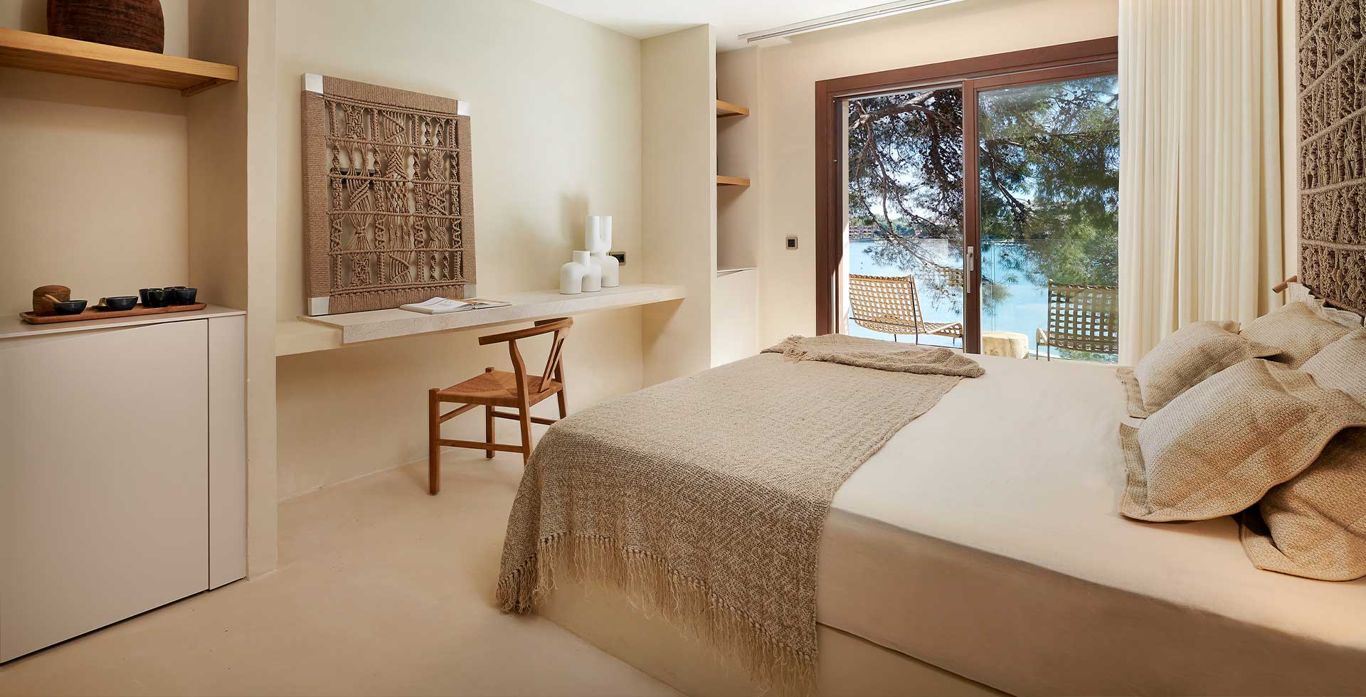 Brightly furnished double room with natural materials and woven elements, featuring a balcony with a view of the bay.