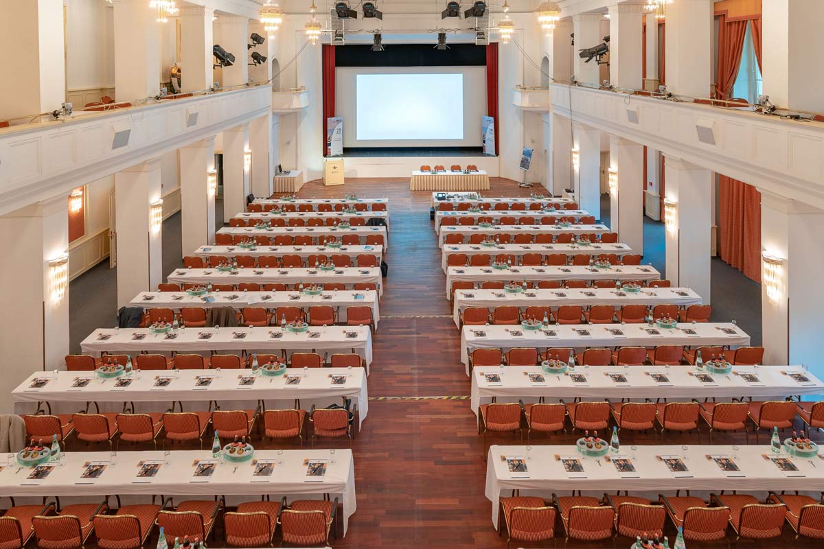 Kaiserbädersaal in the Hotel Kaiserhof Heringsdorf, equipped with long tables, chairs and a large stage.