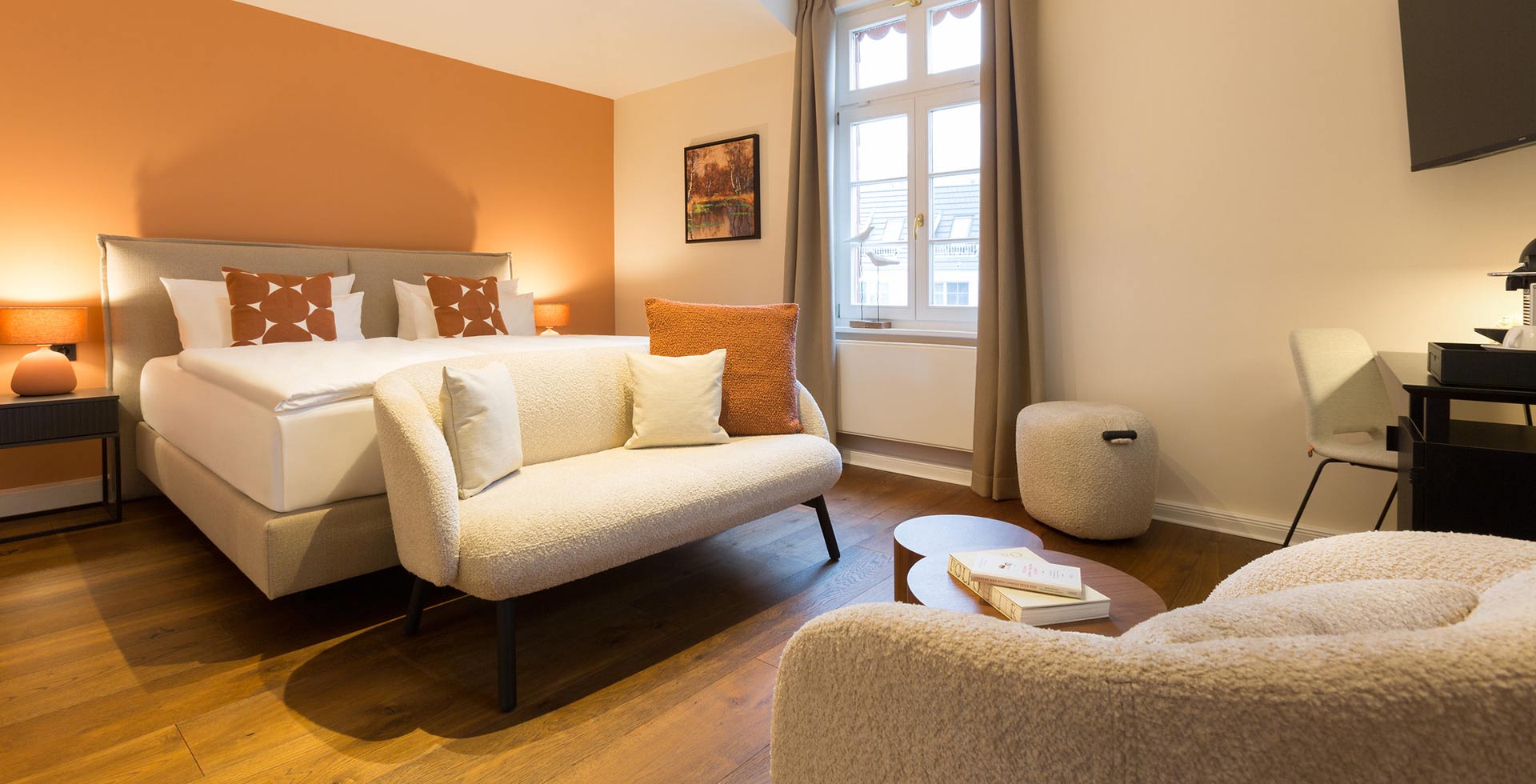 A stylishly furnished double room that combines warm colors and cream tones with wood and soft upholstered elements.